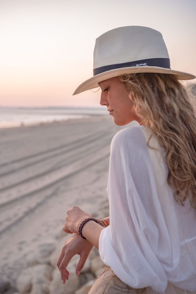Charming woman in hat leaning on fence and looking at sea