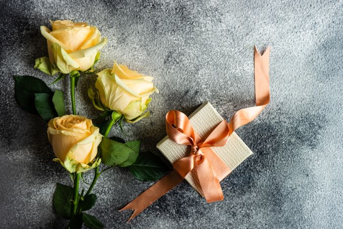Top view of yellow flower on grey table with small present with space for text