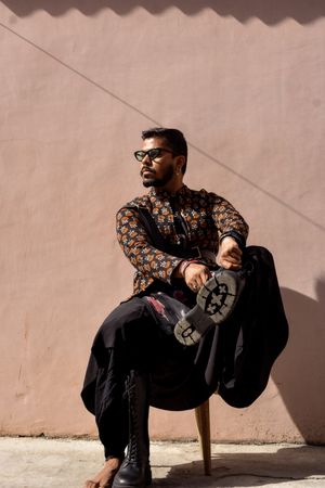 Man wearing kurta sitting on a chair beside wall