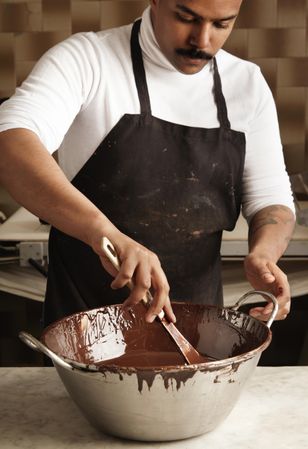 Black male in apron with steel bowl of melted chocolate