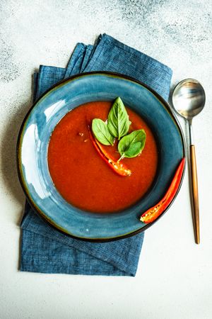 Top view of Spanish soup of tomato gazpacho with basil garnish in blue bowl with spoon