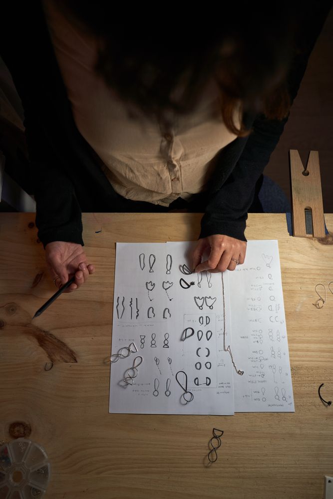 Crop goldsmith working on jewelry illustrations in dark studio