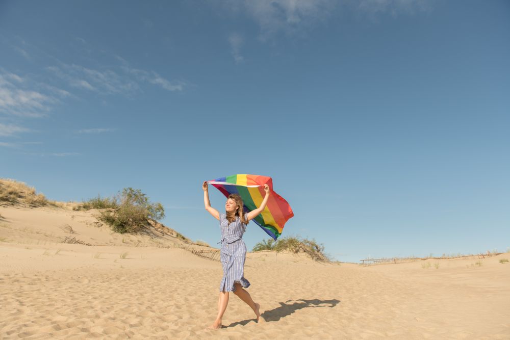 Young woman with rainbow banner against sky