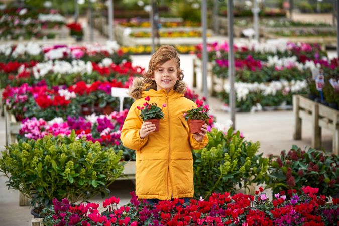 Cheerful preteen boy with blooming potted flowers in garden