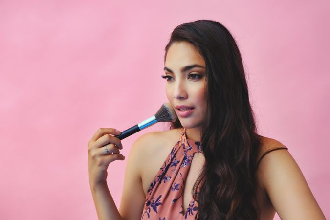 Head shot of elegant Hispanic woman looking away while holding large make up brush