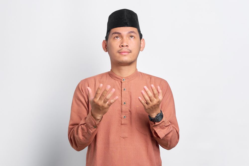 Solemn Muslim man looking up and praying in kufi head wear