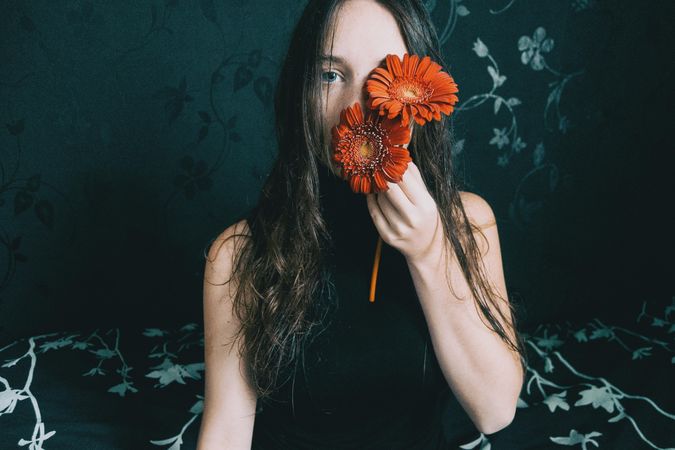 Studio portrait of woman with blue eyes holding gerbera flowers against floral background