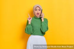 Surprised woman in headscarf holding up finger while talking on phone 0Wp715