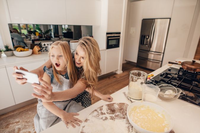 Happy young mother taking selfie with her daughter in kitchen