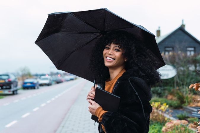 Smiling Black woman with umbrella on street