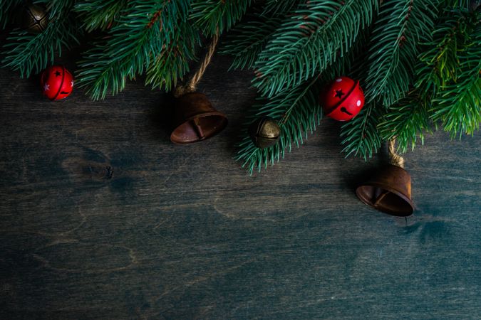 Fir branches on wooden table with red Christmas bells