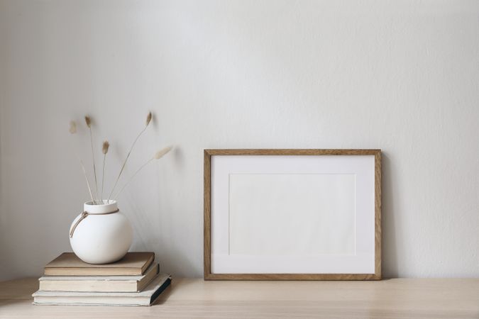 Horizontal blank wooden picture frame mockup on table with vase and books