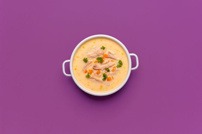 Greek chicken soup above view, minimalist on a purple background