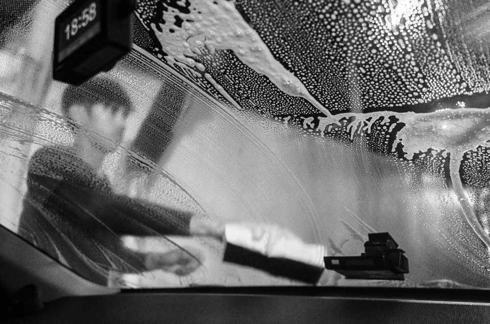 Grayscale photo of man cleaning wind shield of a car
