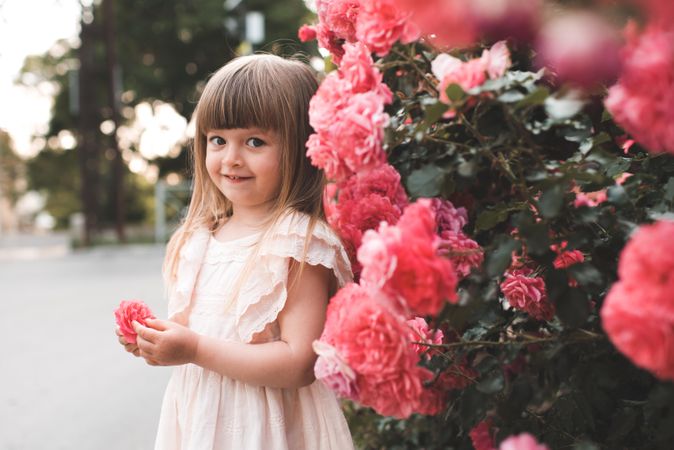 Blonde girl in yellow dress posing with pink rose flowers outdoor