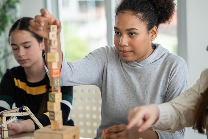 Young teen girl building with wooden blocks on table