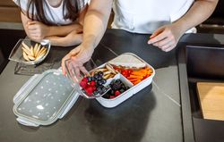 Girl watching her mother putting food in her lunch box