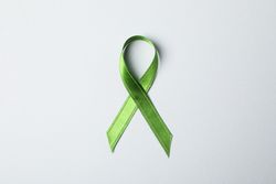 Green awareness ribbon on grey background, space for text
