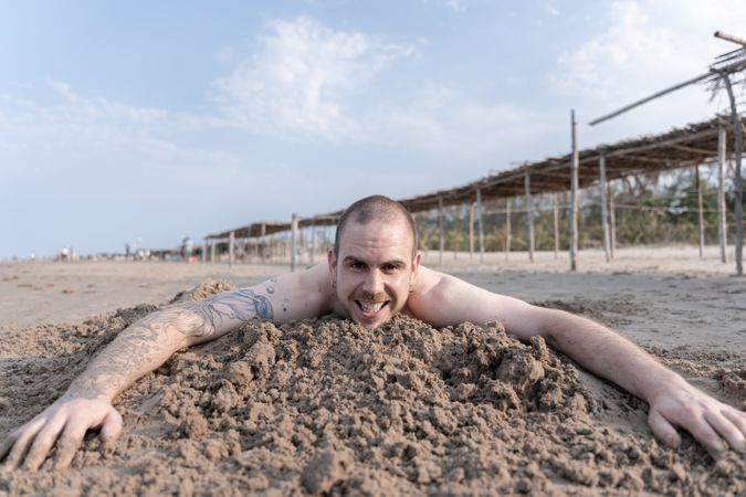 Happy young man enjoying the beach, laying on the sand and smiling at the camera