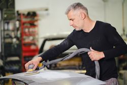 Mechanic grinding paint from car detail