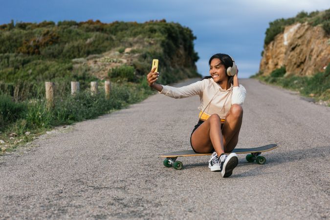 Delightful woman on longboard taking selfie on smartphone