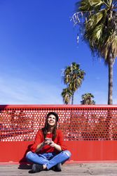 Woman in red sitting cross legged using a mobile phone outdoors on a sunny day