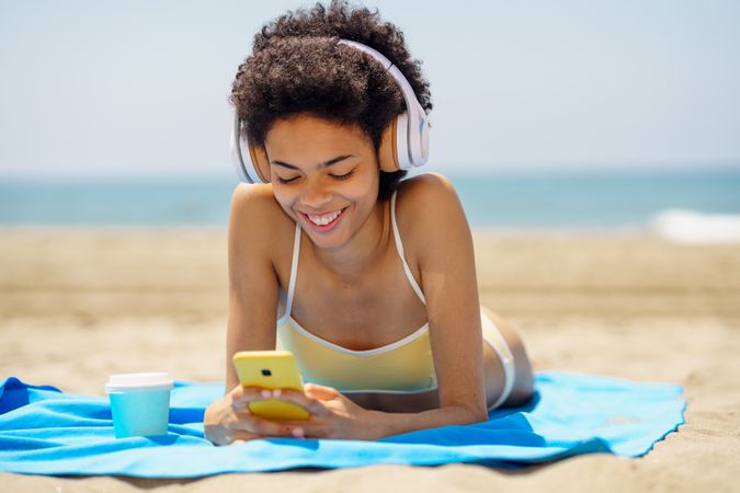 Female with curly hair on beach towel gazing at phone
