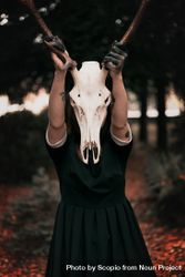 Woman in dark dress holding horse skull with horns 0yO2q4