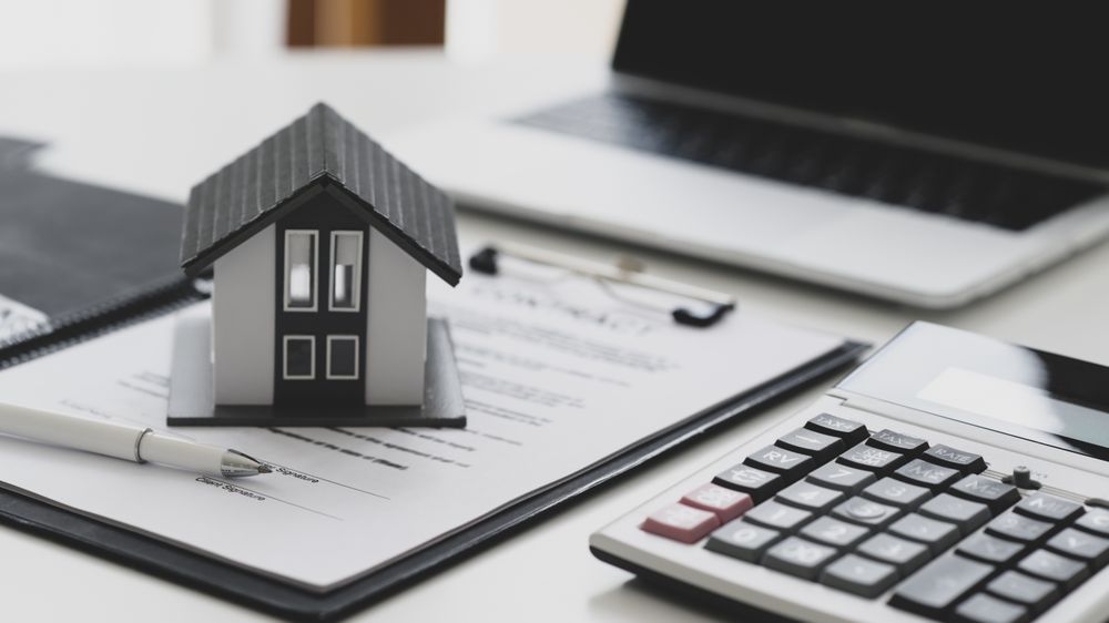 Pen and model house placed on contract documents with calculator and laptop