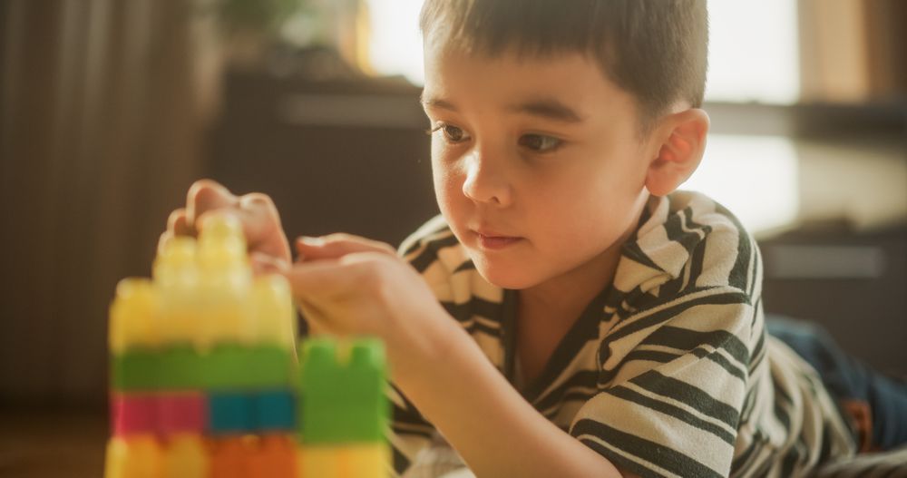 Portrait of Cute Male Asian Child Playing with Colourful Building Blocks in his Room During the Sunny Day.