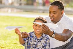 Father and Son Playing with Paper Airplanes in sunny park