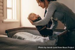 Woman bending forward to put her infant kid in a bedside bassinet 5pP3v5