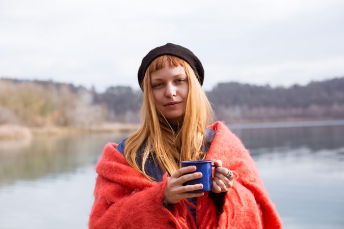 Woman wrapped in warm clothes by the lake holding a mug