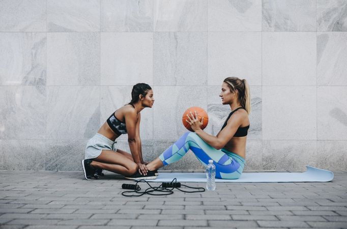 Side view of fitness woman doing sit ups holding a basketball outdoors