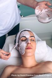 Woman resting with eyes closed while having a clay mask applied bE9gR7