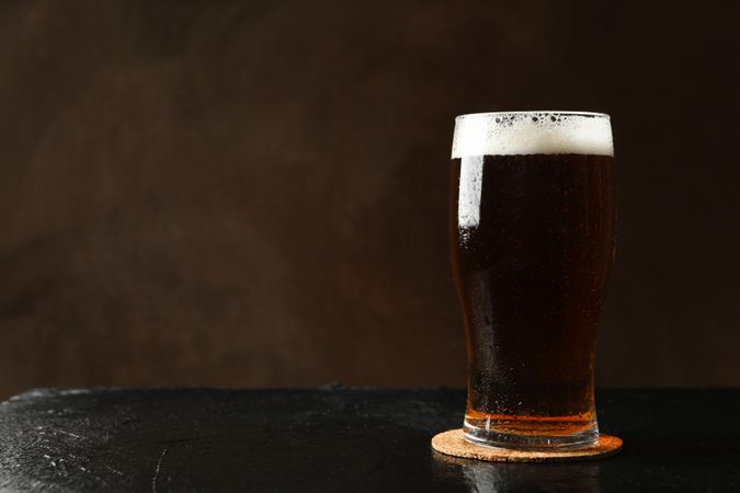 Glass of beer on dark table against brown background