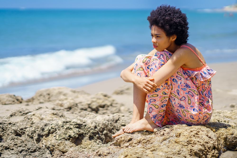 Woman sitting on the rocks on the coast looking out to the sea with head down to knees