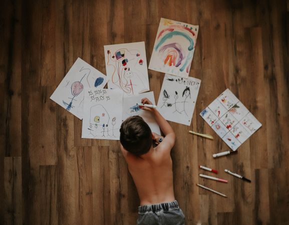 Boy drawing and coloring on paper on floor