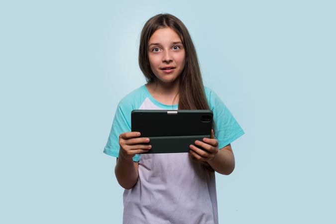Surprised young girl holding tablet, showing shocked expression.