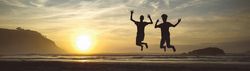 Silhouettes of two kids jumping in the beach at sunset