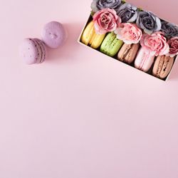 Box of macarons and flowers on pink background