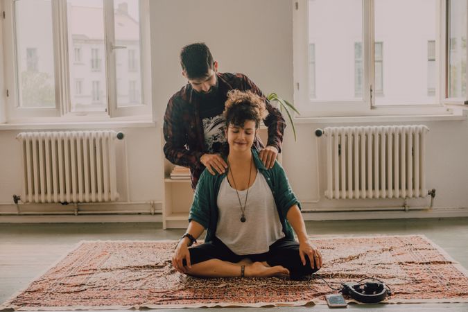 Man rubbing shoulders of joyful woman resting on floor at home