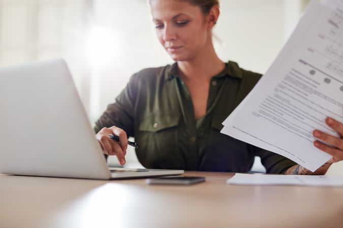 Shot of young woman sitting at table with documents working on laptop computer