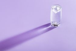 Tonic water with ice cubes in glass on purple background