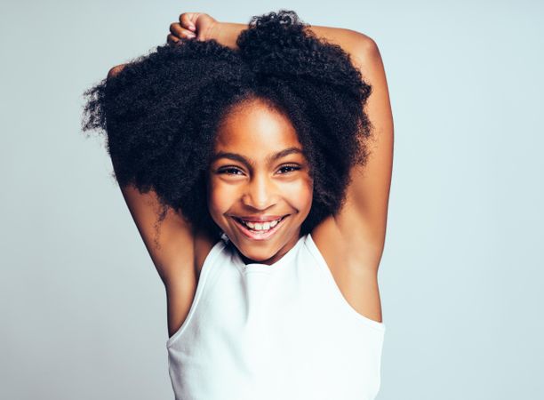 Studio portrait of smiling girl wearing simple vest with arms over her head