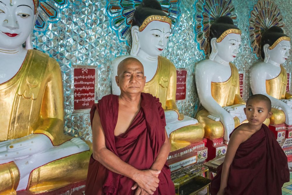 Mandalay, Myanmar - June, 25 2012: Monk and boy near Buddha statues in monastery