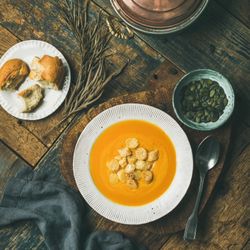 Pumpkin soup with croutons, bread, seeds, spoon on wooden table, square crop