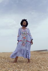 Woman in light dress with floral embroidery standing on yellow grass field