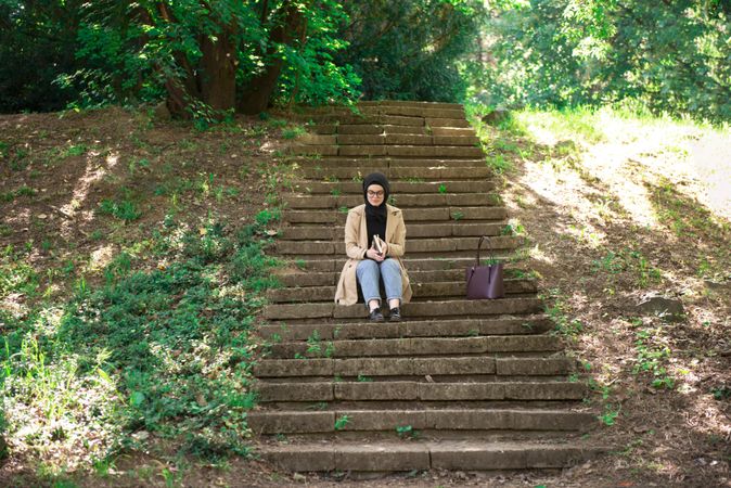 Woman in headscarf reading on park stairs