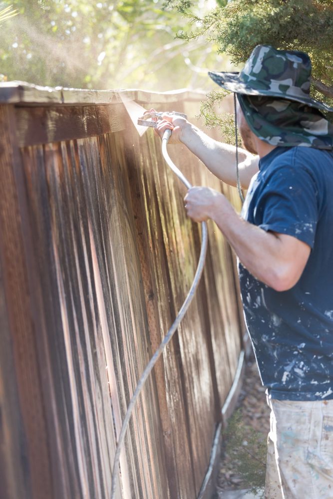 Professional Painter Spraying Yard Fence with Stain